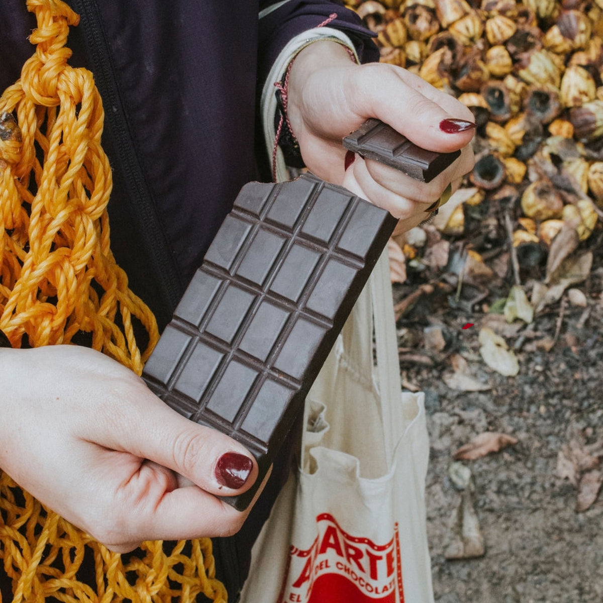 Barra de chocolate AMARTE partida en dos, con cáscaras de mazorca de cacao al fondo y bolsa de tela AMARTE